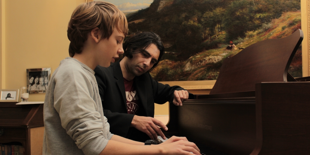 Phil guiding a young pupil at the keys of a grand piano.