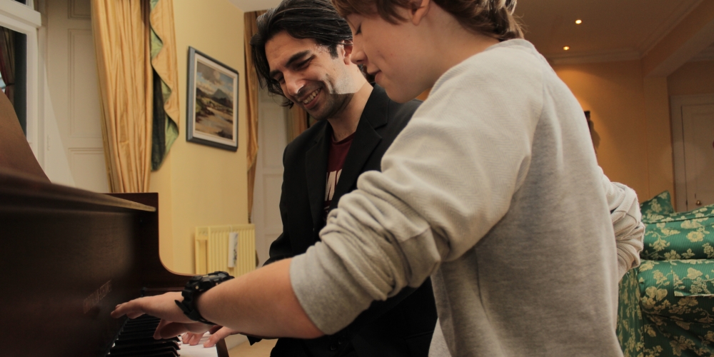Phil smiling beside a young pupil playing the piano at home.